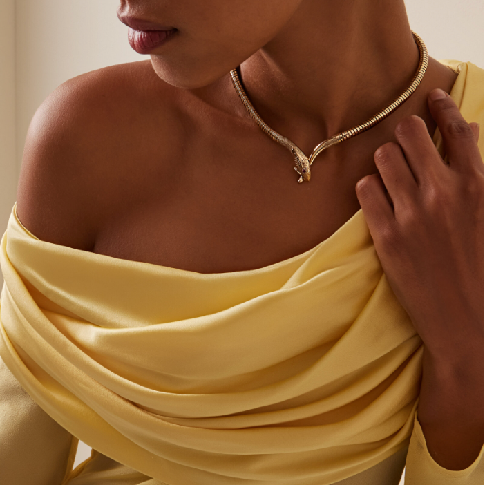 Woman wearing a gold necklace with a yellow top against a neutral background