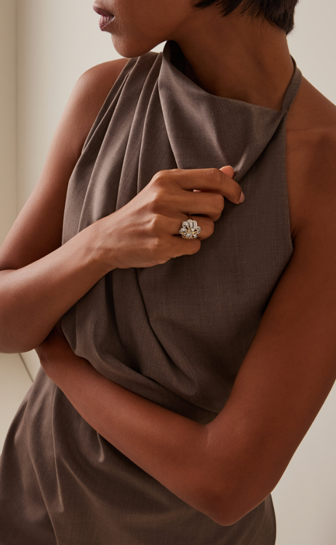 Woman wearing a brown halter top with a ring on her finger against a neutral background