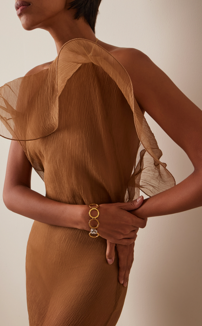 Woman wearing a brown sheer dress with a gold bracelet on a beige background